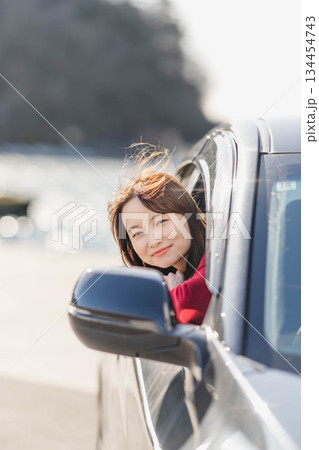 車に乗りながら座席から身を乗り出す赤いニットの若い女性 車に乗りながら座席から身を乗り出す赤いニットの若い女性 134454743