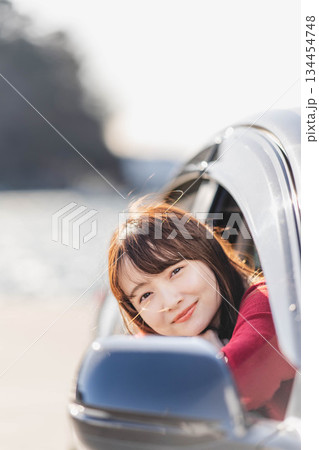 車に乗りながら座席から身を乗り出す赤いニットの若い女性 134454748