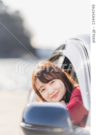 車に乗りながら座席から身を乗り出す赤いニットの若い女性 134454749