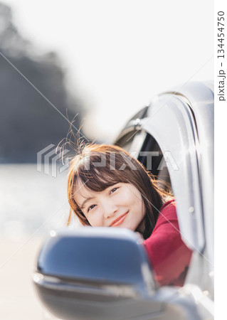 車に乗りながら座席から身を乗り出す赤いニットの若い女性 134454750