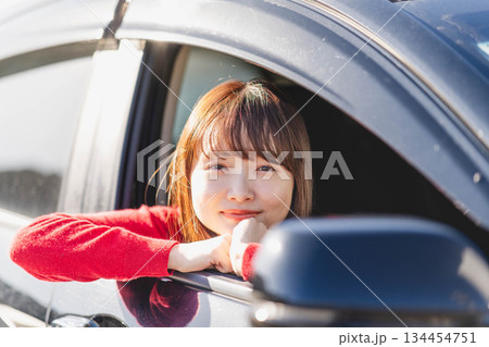 車に乗りながら座席から身を乗り出す赤いニットの若い女性 車に乗りながら座席から身を乗り出す赤いニットの若い女性 134454751