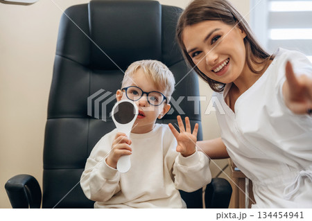 Sitting with doctor. Little boy is having check up in the ophthalmologist cabinet Sitting with doctor. Little boy is having check up in the ophthalmologist cabinet 134454941