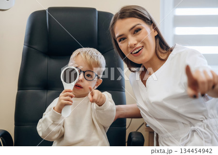 Sitting with doctor. Little boy is having check up in the ophthalmologist cabinet 134454942