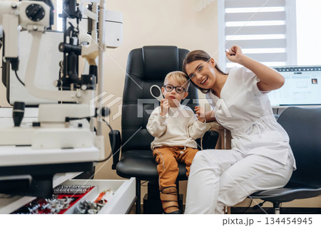 Sitting with doctor. Little boy is having check up in the ophthalmologist cabinet 134454945