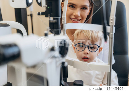 By the modern device. Little boy is having check up in the ophthalmologist cabinet By the modern device. Little boy is having check up in the ophthalmologist cabinet 134454964