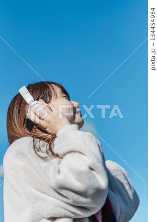 青空の下に立ち音楽を聴く笑顔の女の子 青空の下に立ち音楽を聴く笑顔の女の子 134454984