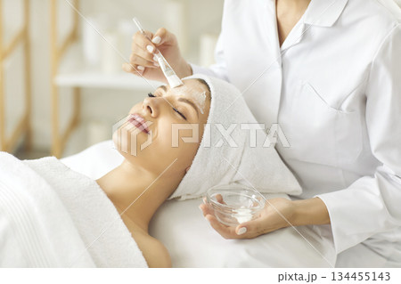 Beautician doing facial treatment and applying beauty mask on face of young woman Beautician doing facial treatment and applying beauty mask on face of young woman 134455143