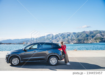 青空のもと冬の海で車に寄りかかって休憩するロングヘアの若い女性 青空のもと冬の海で車に寄りかかって休憩するロングヘアの若い女性 134455457