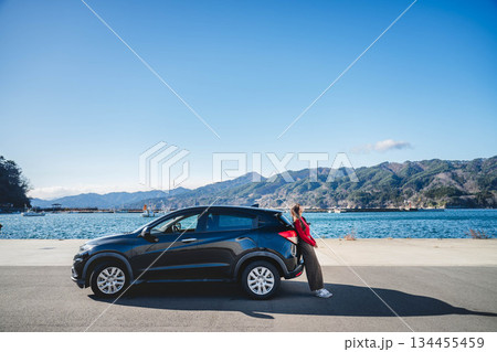青空のもと冬の海で車に寄りかかって休憩するロングヘアの若い女性 青空のもと冬の海で車に寄りかかって休憩するロングヘアの若い女性 134455459