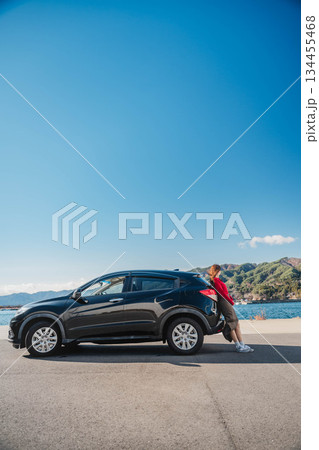 青空のもと冬の海で車に寄りかかって休憩するロングヘアの若い女性 青空のもと冬の海で車に寄りかかって休憩するロングヘアの若い女性 134455468