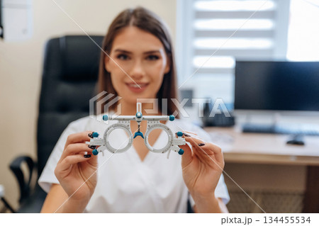The professional eyewear for measuring sight sharpness. Young female ophthalmologist is in the cabinet The professional eyewear for measuring sight sharpness. Young female ophthalmologist is in the cabinet 134455534