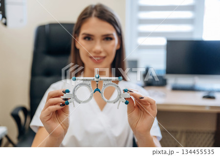 The professional eyewear for measuring sight sharpness. Young female ophthalmologist is in the cabinet The professional eyewear for measuring sight sharpness. Young female ophthalmologist is in the cabinet 134455535