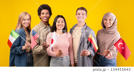 Friends, team, international language course and modern education. Happy young multiracial students holding flags of their countries isolated on orange background, copy space, studio shot 134455643