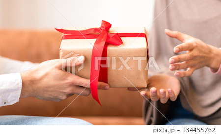 Muslim Husband Giving Gift Box To Wife, Closeup Of Hands, Celebrating Valentine's Day Together Sitting Indoors. Valentine And Birthday Holiday Celebration, Gifts And Presents. Cropped 134455762