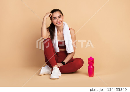 Fitness And Healthy Lifestyle Concept. Happy sporty young woman sitting on the floor with bottle of water at studio after exercising, resting and looking at camera. Wellness And Training Fitness And Healthy Lifestyle Concept. Happy sporty young woman sitting on the floor with bottle of water at studio after exercising, resting and looking at camera. Wellness And Training 134455849