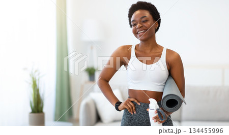 African Fit Woman Holding Yoga Mat And Sport Water Bottle Standing At Home, Smiling To Camera. Domestic Training. Ready For Fitness Workout Concept. Sporty People Lifestyle African Fit Woman Holding Yoga Mat And Sport Water Bottle Standing At Home, Smiling To Camera. Domestic Training. Ready For Fitness Workout Concept. Sporty People Lifestyle 134455996
