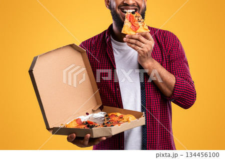 Happy African Man Eating Pizza Smiling To Camera Standing Over Yellow Studio Background. Junk Food Eater Enjoying Unhealthy Pizza. Nutrition And Cheat Meal, Fastfood Overeating Habit Happy African Man Eating Pizza Smiling To Camera Standing Over Yellow Studio Background. Junk Food Eater Enjoying Unhealthy Pizza. Nutrition And Cheat Meal, Fastfood Overeating Habit 134456100