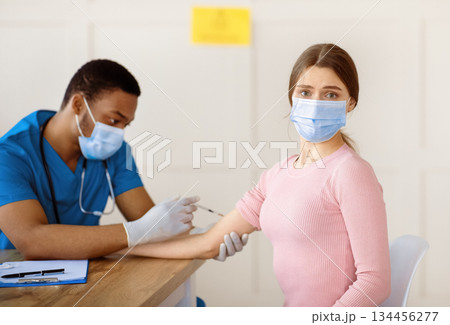 Unhappy young woman in face mask feeling afraid of pain during covid-19 vaccine shot at medical office. Millennial female patient getting immunization against global infectious disease Unhappy young woman in face mask feeling afraid of pain during covid-19 vaccine shot at medical office. Millennial female patient getting immunization against global infectious disease 134456277