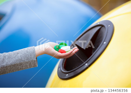 Unrecognizable Woman Throwing Handful Of Colorful Plastic Lids Bottle Caps Into Yellow Recycle Bin, Enjoying Garbage Sorting And Zero Waste Living, Cropped Image With Selective Focus, Free Space Unrecognizable Woman Throwing Handful Of Colorful Plastic Lids Bottle Caps Into Yellow Recycle Bin, Enjoying Garbage Sorting And Zero Waste Living, Cropped Image With Selective Focus, Free Space 134456356