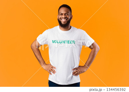 Cheerful African Volunteer Guy Standing With His Hands On Hips Ready For Voluntary Work Posing On Yellow Studio Background, Smiling To Camera. Volunteering Job, Activist's Portrait Concept Cheerful African Volunteer Guy Standing With His Hands On Hips Ready For Voluntary Work Posing On Yellow Studio Background, Smiling To Camera. Volunteering Job, Activist's Portrait Concept 134456392
