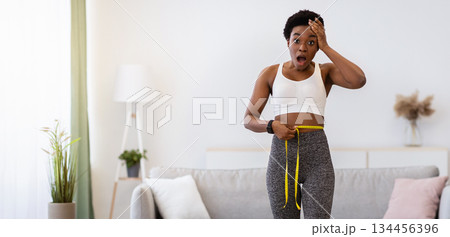 Slimming Failure. Shocked African American Lady Weighing After Weight Gain And Measuring Waist With Tape Standing On Scales Indoors, Looking At Camera In Shock. Full Length Slimming Failure. Shocked African American Lady Weighing After Weight Gain And Measuring Waist With Tape Standing On Scales Indoors, Looking At Camera In Shock. Full Length 134456396