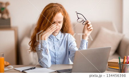 Tired red-haired schoolgirl rubbing dry irritated eyes, studying online on laptop at home, free space. Teen female student exhausted from looking at screen, doing assignments or communicating on web Tired red-haired schoolgirl rubbing dry irritated eyes, studying online on laptop at home, free space. Teen female student exhausted from looking at screen, doing assignments or communicating on web 134456398
