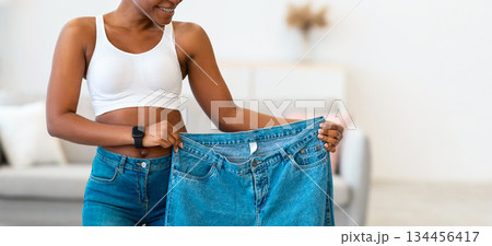 Joy Of Weight Loss. Black Lady Holding Oversized Jeans Too Big After Great Weight-Loss And Successful Slimming Standing Posing At Home. Dieting Motivation Concept Joy Of Weight Loss. Black Lady Holding Oversized Jeans Too Big After Great Weight-Loss And Successful Slimming Standing Posing At Home. Dieting Motivation Concept 134456417