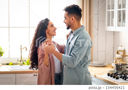 Portrait Of Happy Affectionate Arab Spouses Bonding Together In Kitchen, Loving Middle Eastern Man And Woman Holding Hands And Smiling To Each Other, Having Romantic Moments At Home, Free Space 134456421