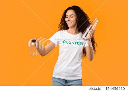 No More Plastic. Female Volunteer Choosing Between Glass And Plastic Bottle Posing Standing In Studio Over Yellow Background. Stop Using Single-Used Bottles, Ecology Concept No More Plastic. Female Volunteer Choosing Between Glass And Plastic Bottle Posing Standing In Studio Over Yellow Background. Stop Using Single-Used Bottles, Ecology Concept 134456430