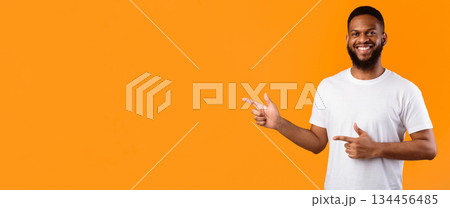 African Guy Pointing Fingers Aside Standing Over Yellow Studio Background, Smiling To Camera, Advertising Your Text. Look There, Advertisement Banner. Panorama, Blank Space 134456485
