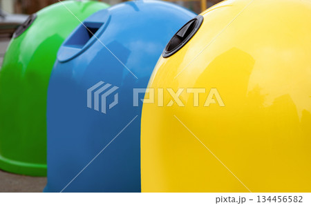 Waste Sorting Concept. Closeup Shot Of Colorful Garbage Containers For Different Sort Of Materials Standing Outdoors, Yellow Blue And Green Trash Bin For Diverse Kind Of Trash For Recycling Waste Sorting Concept. Closeup Shot Of Colorful Garbage Containers For Different Sort Of Materials Standing Outdoors, Yellow Blue And Green Trash Bin For Diverse Kind Of Trash For Recycling 134456582