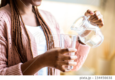 Smiling African American Woman Pouring Water From Jug To Glass. Unrecognizable Black Female Drinking Healthy Liquid In Kitchen, Enjoying Refreshing Drink, Cropped Image, Closeup Shot 134456638