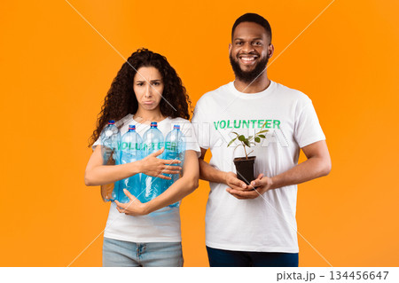 Don't Litter And Care For Nature. Two Volunteers Holding Plant In A Pot And Used Plastic Bottles Standing Over Yellow Studio Background. Ecology, Protection Of Environment Concept 134456647