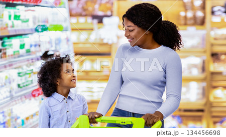 Young black mom and her daughter shopping together for groceries, choosing dairy products at store. Millennial African American family with cart purchasing food at big hypermarket Young black mom and her daughter shopping together for groceries, choosing dairy products at store. Millennial African American family with cart purchasing food at big hypermarket 134456698