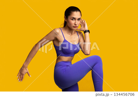 High-Intensity Interval Training. Portrait Of Confident Sporty Young Woman Lifting Leg Up, Raising Arm, Doing High Knee Cardiovascular Exercise Standing Isolated On Orange Studio Background High-Intensity Interval Training. Portrait Of Confident Sporty Young Woman Lifting Leg Up, Raising Arm, Doing High Knee Cardiovascular Exercise Standing Isolated On Orange Studio Background 134456706