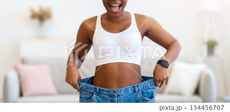 Weight Loss. Joyful Slim African American Lady Wearing Old Large Jeans Showing Result Of Slimming Standing Indoors. Motivation And Comparison, Successful Dieting And Weight-Loss Concept 134456707
