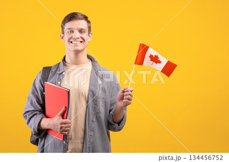 Canada day, patriotism and knowledge sharing. Millennial smiling european guy in casual with backpack, notepads and small flag, isolated on orange background, cut out, copy space, studio shot Canada day, patriotism and knowledge sharing. Millennial smiling european guy in casual with backpack, notepads and small flag, isolated on orange background, cut out, copy space, studio shot 134456752
