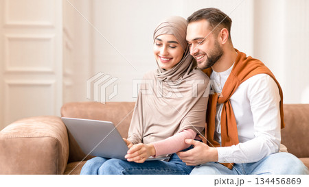 Happy Married Arab Couple Watching Movie On Laptop Sitting And Hugging On Sofa In Living Room At Home. Weekend Leisure And Relaxation. Muslim Spouses Browsing Internet Together Happy Married Arab Couple Watching Movie On Laptop Sitting And Hugging On Sofa In Living Room At Home. Weekend Leisure And Relaxation. Muslim Spouses Browsing Internet Together 134456869