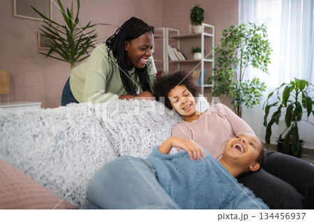Mother and daughters laughing on couch at home 134456937