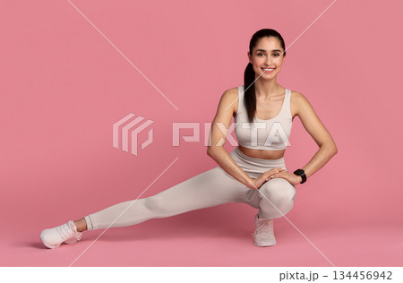 Leg And Glute Training. Smiling Fit Young Lady In Sportswear Doing Deep Side Squat Exercise During Workout, Warming Up, Isolated On Pink Studio Background. Full Length, Copy Space. Fitness And Sport. Leg And Glute Training. Smiling Fit Young Lady In Sportswear Doing Deep Side Squat Exercise During Workout, Warming Up, Isolated On Pink Studio Background. Full Length, Copy Space. Fitness And Sport. 134456942