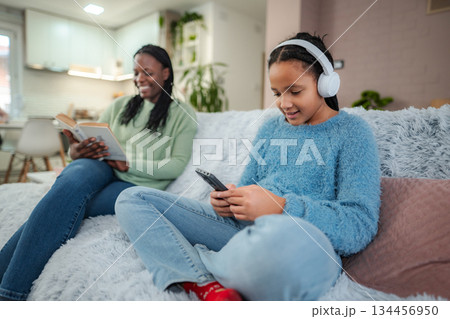 Mother and daughter using different technologies for leisure time on sofa 134456950