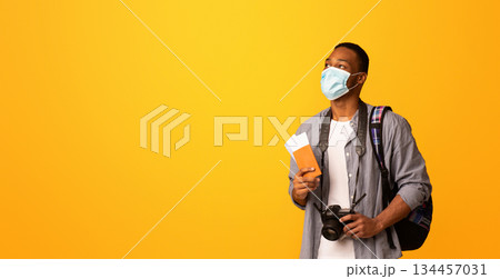 New Travel Rules. Young Black Tourist Man In Medical Face Mask Looking Aside At Copy Space, African Guy With Passport And Photo Camera Ready For Trip During Coronavirus Pandemic, Yellow Background 134457031