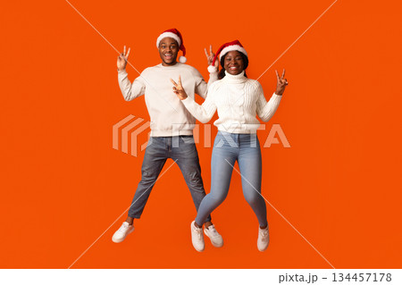 Joyful African American Spouses In Santa Hats Jumping And Showing Peace Gesture, Having Fun Together Over Orange Studio Background, Black Couple Enjoying Celebrating Christmas Holidays, Copy Space Joyful African American Spouses In Santa Hats Jumping And Showing Peace Gesture, Having Fun Together Over Orange Studio Background, Black Couple Enjoying Celebrating Christmas Holidays, Copy Space 134457178