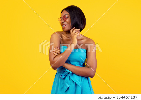 Summer fashion. Lovely black lady in beautiful blue dress and sunglasses posing and smiling on orange studio background. Sexy African American woman wearing stylish summertime outfit 134457187