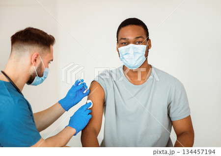 Immunization and health care system. Black male patient visiting doctor, receiving covid-19 vaccine injection at clinic. Medical worker vaccinating young man from coronavirus 134457194