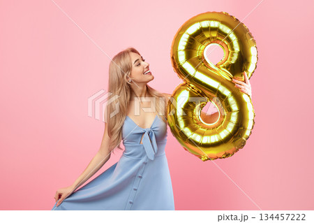 8th March celebration concept. Portrait of lovely blonde lady in dress holding number eight golden balloon for Woman's Day on pink studio background, copy space 8th March celebration concept. Portrait of lovely blonde lady in dress holding number eight golden balloon for Woman's Day on pink studio background, copy space 134457222