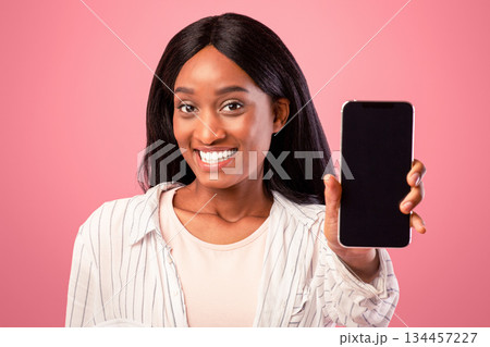Pretty black woman showing mobile phone with space for your app design, pink studio background. Lovely African American lady holding smartphone with mockup for website. Communications concept Pretty black woman showing mobile phone with space for your app design, pink studio background. Lovely African American lady holding smartphone with mockup for website. Communications concept 134457227