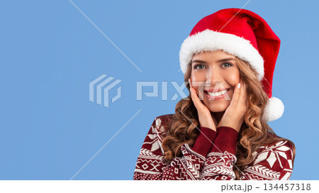 Portrait of lovely young girl in Christmas sweater and Santa hat smiling on blue background. Panorama Portrait of lovely young girl in Christmas sweater and Santa hat smiling on blue background. Panorama 134457318