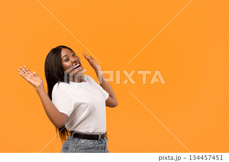 Excited young black woman raising hands up, standing by copy space for text or advertisement, orange studio background. Amazed african american lady and empty space for advertising Excited young black woman raising hands up, standing by copy space for text or advertisement, orange studio background. Amazed african american lady and empty space for advertising 134457451