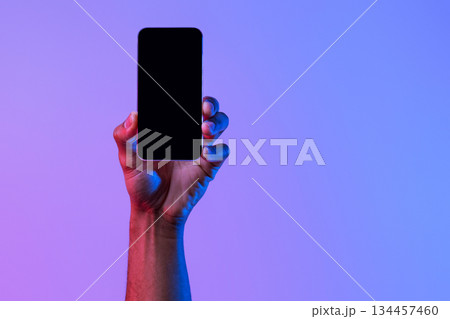 Social network and modern technology. Female hand holds phone with blank screen on neon background, close up, copy space Social network and modern technology. Female hand holds phone with blank screen on neon background, close up, copy space 134457460